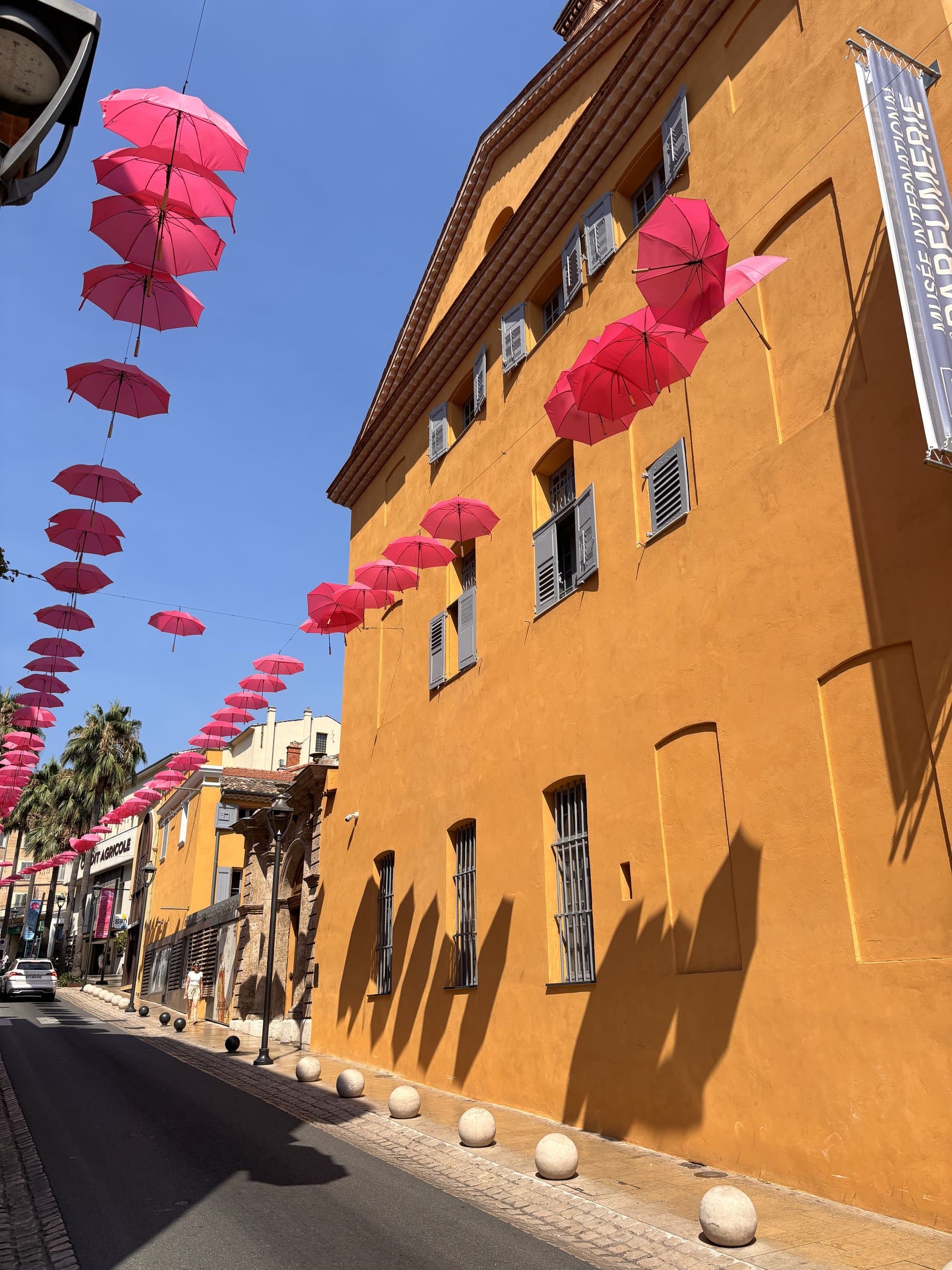 Ochre façade of the International Perfume Museum in Grasse, under a canopy of pink umbrellas